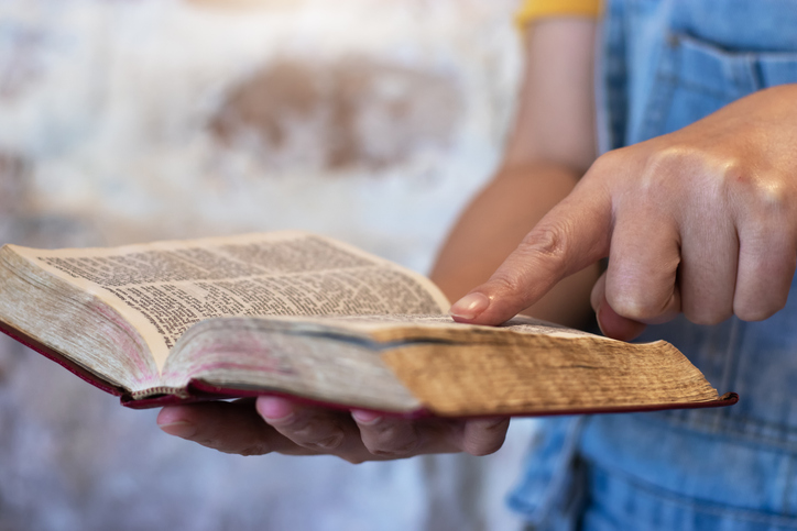 Closeup of an unrecognizable person's hands held over a bible at home during the day - stock photo