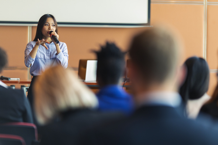 woman speaking into a microphone in front of a crowd