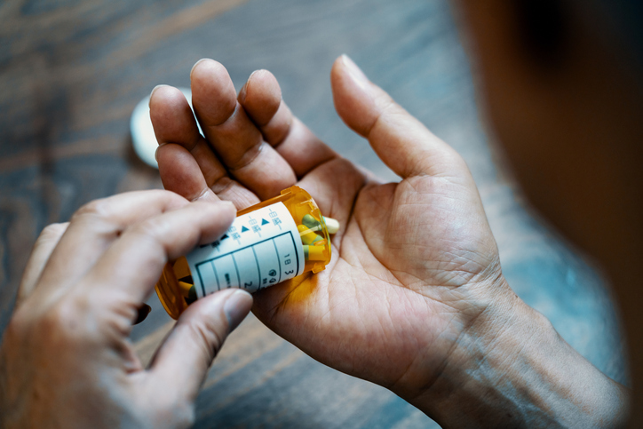 Close-up of a male hand holding a pill bottle pouring medication into his hand - stock photo